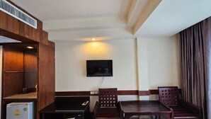 A compact room with a wooden cabinet, a small refrigerator, a flat-screen TV mounted on the wall, and a dining table with four chairs. - Boutique Bravo Hotel (Pattaya)