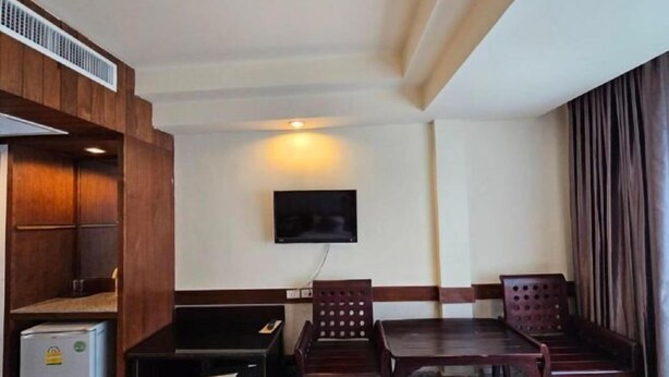 Una camera compatta con un armadio in legno, un piccolo frigorifero, una TV a schermo piatto montata a parete e un tavolo da pranzo con quattro sedie.
