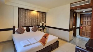 Una habitación de hotel con una cama grande, una mesita de noche, un cabecero de madera y una puerta que da a otra habitación.