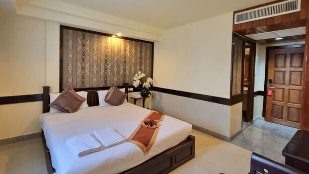 Een hotelkamer met een groot bed, een nachtkastje, een houten hoofdbord en een deur naar een andere kamer.