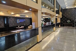 Un espace d’accueil d’hôtel comprenant un comptoir de réception, un écran numérique et un panneau indiquant que l’établissement est non-fumeur.