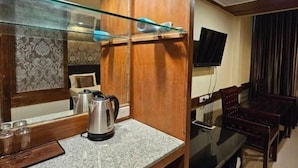 A hotel room with a wooden cabinet, a glass shelf, a kettle, a TV, and a dining area with chairs and a table. - Boutique Bravo Hotel (Pattaya)