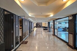 Un couloir d’hôtel au design moderne, avec un long couloir, des portes en verre et un comptoir d’accueil situé au fond.