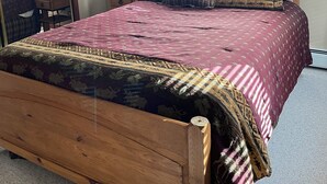 Un dormitorio con cama de madera, cortinas oscuras, ventilador de techo, mesita de noche con lámpara y espejo.