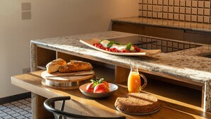 Ein Frühstücksbuffet mit Brot, Tomaten, einem Teller mit Speisen und einem Krug Orangensaft auf einer Küchenarbeitsplatte.