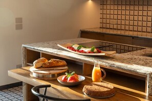 A breakfast setup with bread, tomatoes, a plate of food, and a jug of orange juice on a kitchen counter.