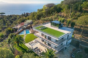 A modern two-story house with a rooftop garden, a swimming pool, and a view of the sea.