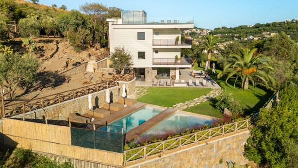Une maison moderne à deux étages, dotée d’une piscine, d’un espace salon extérieur et offrant une vue sur le paysage environnant.