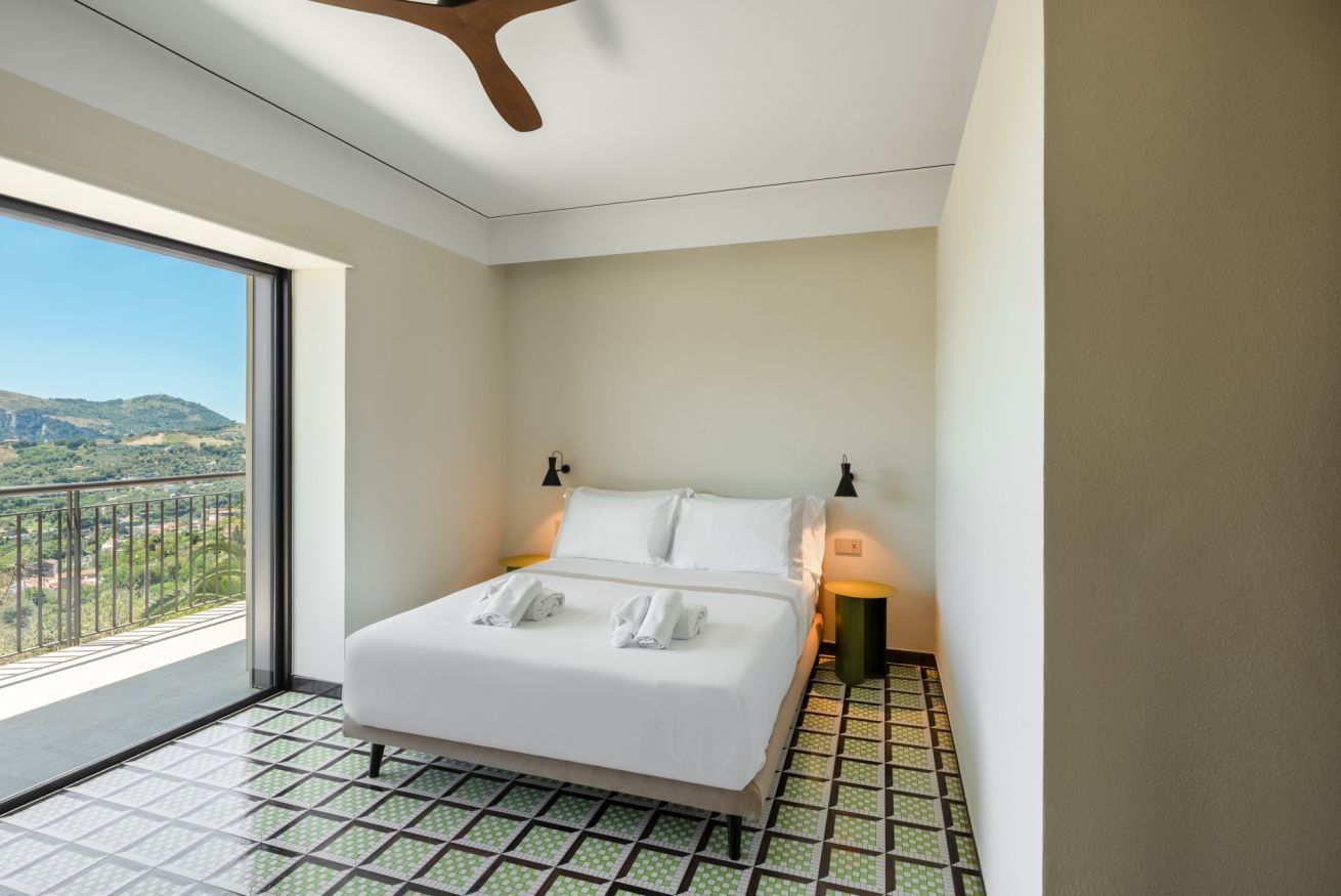 Een hotelkamer met een groot raam, een bed, twee bedlampen en uitzicht op de omgeving.