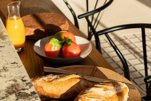 Une table avec du pain, des tomates et un verre de jus d’orange.