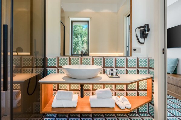 A bathroom with a large white sink, a mirror, and a window. There are towels on a wooden shelf and a hairdryer on the wall.