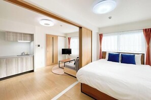 A modern hotel room with a bed, a desk, a TV, and a kitchenette. - TASUKI smart Higashinakano (Tokyo)