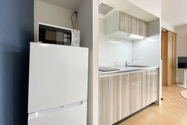 A modern kitchen with a white refrigerator, a built-in microwave, a sink, and wooden cabinets. - TASUKI smart Higashinakano (Tokyo)