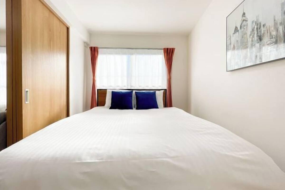 Una camera d'albergo con un letto grande, un armadio in legno, una finestra con tende e un quadro raffigurante un panorama urbano.