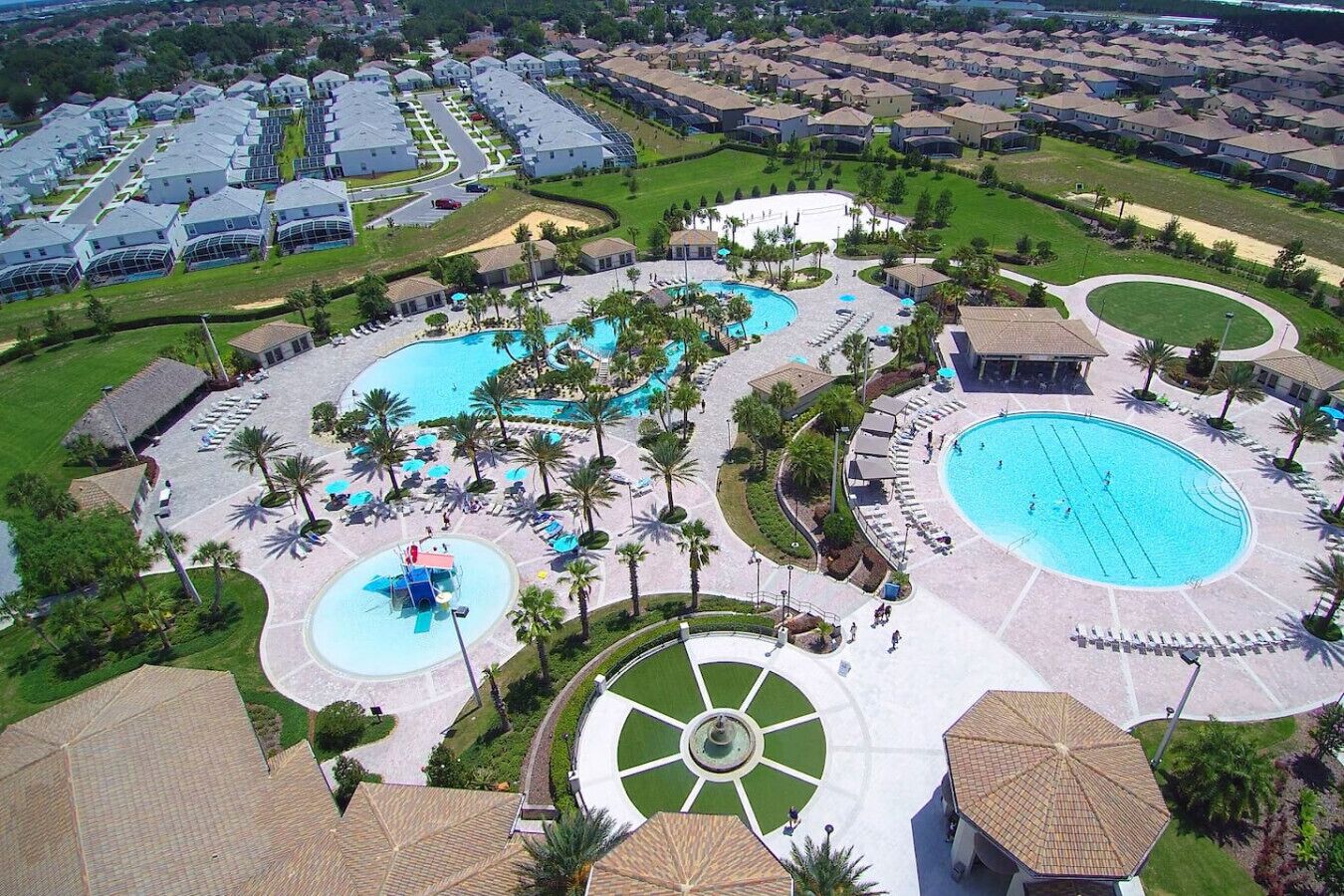 Ein Luftbild eines Resorts mit mehreren Schwimmbecken, Palmen und einer zentralen Fontäne.