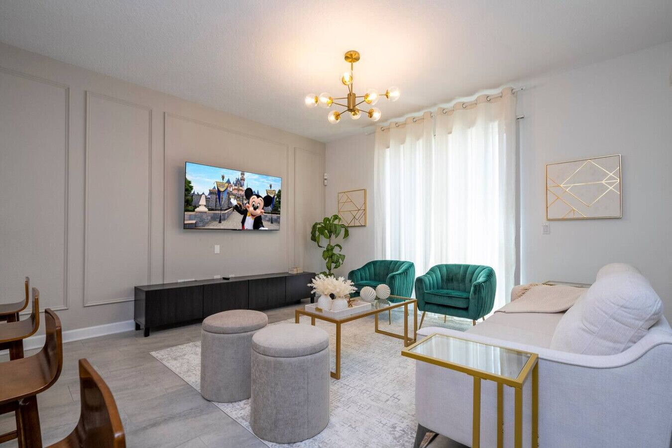 Ett modernt vardagsrum med en platt-TV, turkosa fåtöljer, en vit soffa och ett soffbord.
