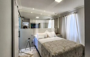 Una habitación de hotel moderna con una cama grande, un espejo, un televisor y una pequeña mesa con una planta.