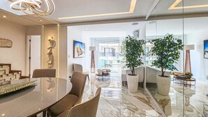 A modern dining area with a glass table, chairs, and a decorative light fixture. There are potted plants and a view of the cityscape through large windows. - Apartment in Guarujá, 7 minutes from the beach (Guarujá)