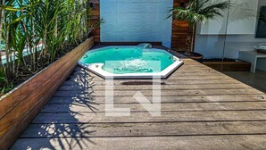 A wooden deck with a hot tub in the center, surrounded by potted plants and a wooden fence. - Apartment in Guarujá, 7 minutes from the beach (Guarujá)