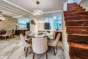 A modern dining area with a glass table, cushioned chairs, and a wooden staircase.