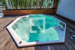 Un jacuzzi en una terraza de madera con una jardinera de madera y una barandilla metálica al fondo.