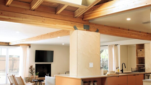 Una cocina moderna con vigas de madera, una isla integrada y un televisor sobre la chimenea.