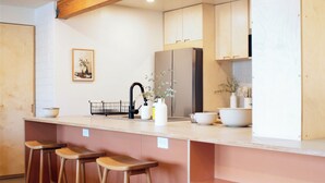 Una cocina con vigas de madera, un lavamanos, taburetes y un refrigerador.