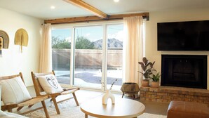 Una sala de estar con chimenea, televisor montado en la pared y un amplio ventanal corredero que da a un espacio exterior.