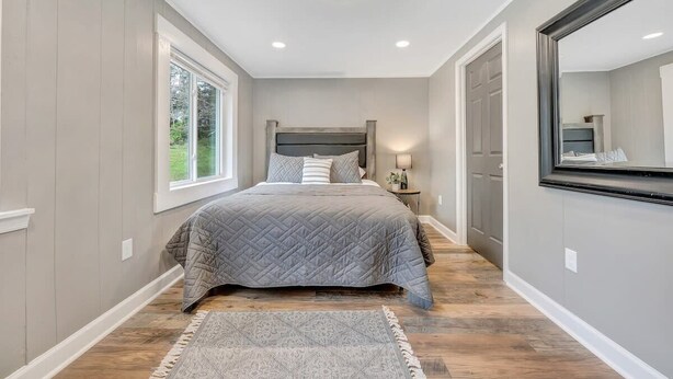 A bedroom with a large bed, a nightstand, a mirror, and a window. - Cottage in the Pines (Rocky Mount)