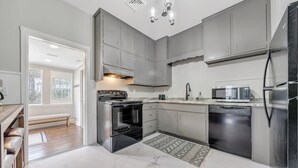 A modern kitchen with grey cabinets, a built-in oven, a microwave, and a dishwasher. - Cottage in the Pines (Rocky Mount)
