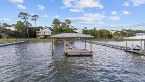 Un muelle se adentra en aguas tranquilas, con un pabellón cubierto y una casa al fondo.