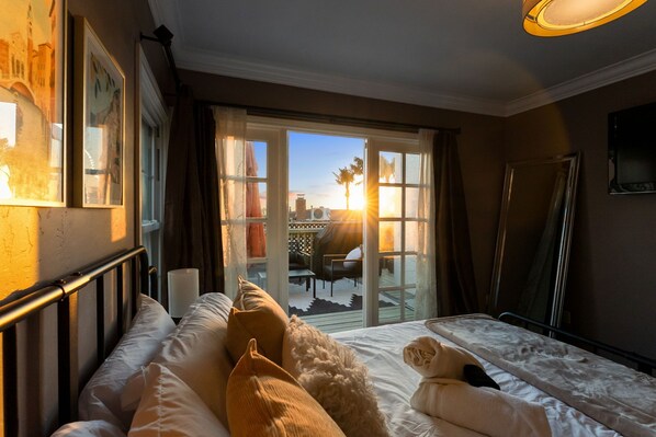Quarto de hotel com cama, uma janela grande com cortinas, vista para o exterior e um espelho na parede.