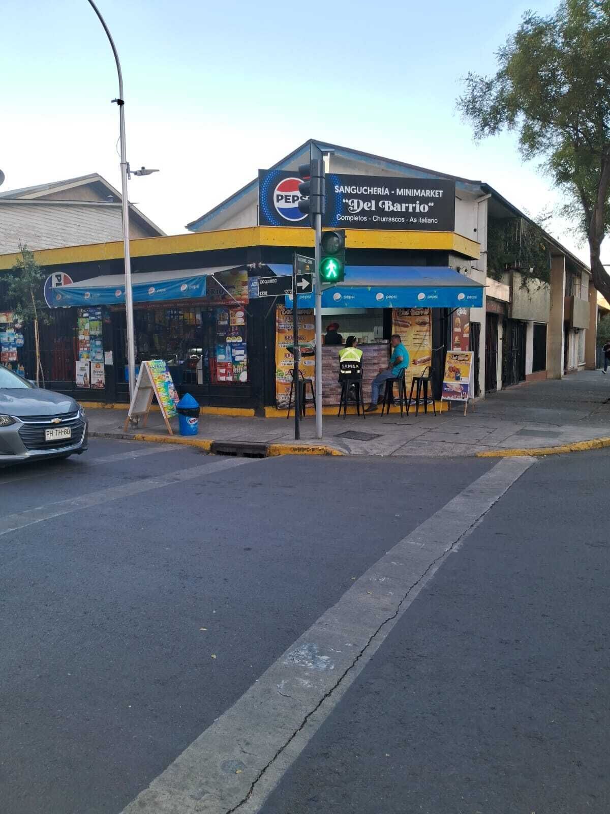 Esquina de rua com um prédio exibindo um letreiro da Pepsi, faixa de pedestres e placa de rua visível.