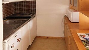 Ett smalt kök med vita skåp, en svart spis och en träbänkskiva med en vattenkokare.