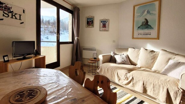 Ett mysigt rum med ett träbord, en soffa och en tv som står på ett stativ.