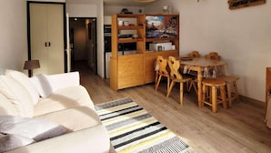 Ett mysigt vardagsrum med en soffa, ett matbord med stolar, en köksdel med träskåp och en tv-apparat på ett träbord.