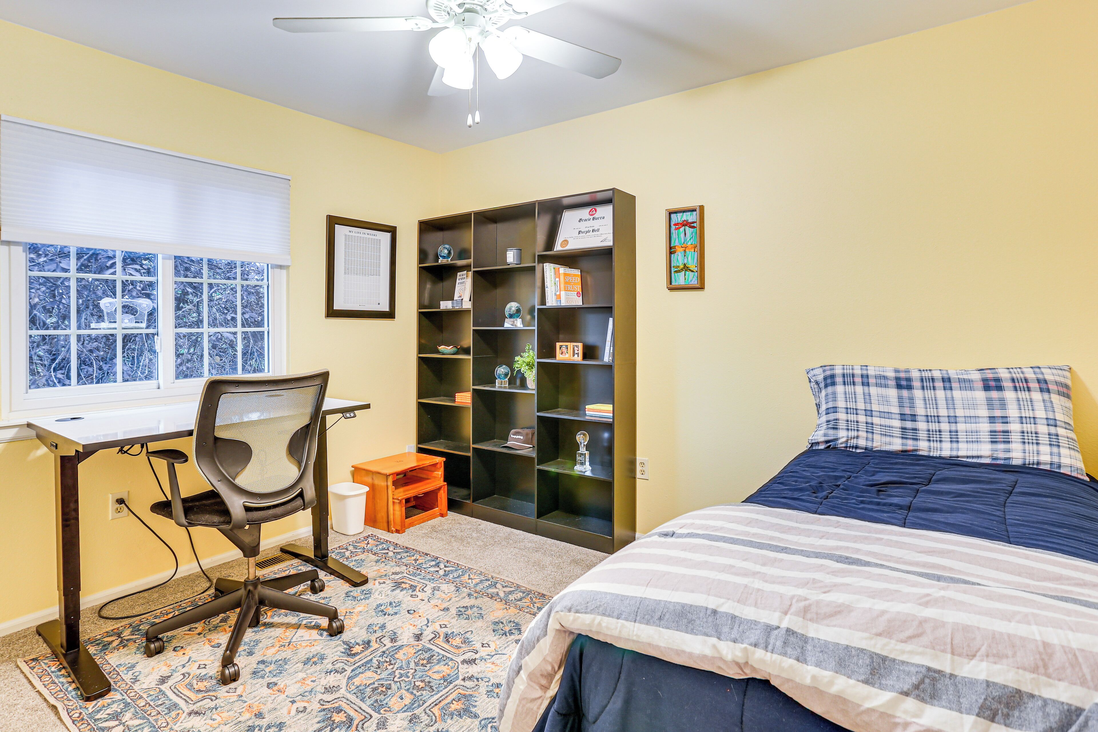 A bedroom with a bed, a desk with a chair, a bookshelf, and a window.