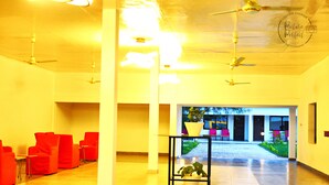 A spacious lobby with red chairs, a black table with potted plants, and ceiling fans. - The Haven Sun N' Fun Hotel (Tanji)