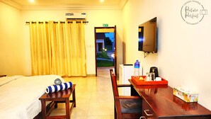 A hotel room with a bed, a desk, a chair, a TV, and a window with curtains. - The Haven Sun N' Fun Hotel (Tanji)