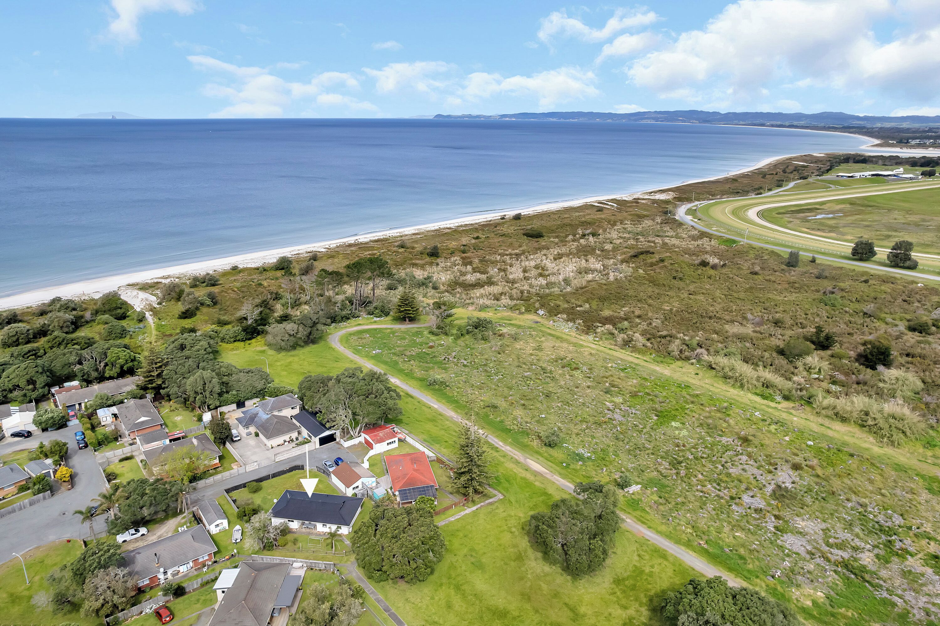 Vue aérienne d’une zone côtière avec une route sinueuse, une plage et un quartier résidentiel avec des maisons et de la végétation.