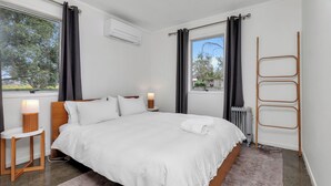 Une chambre avec un grand lit, des tables de chevet avec des lampes, une fenêtre avec des rideaux et un radiateur.