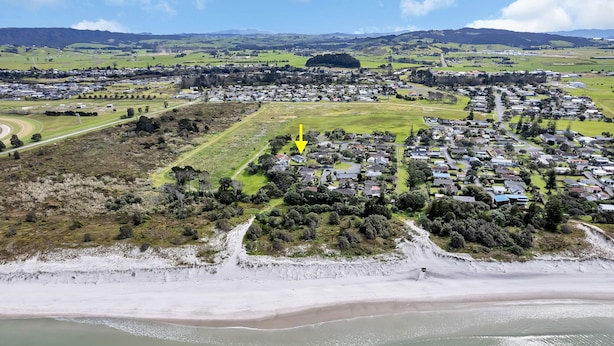 Une vue aérienne d’une ville côtière, avec une plage, des zones résidentielles et un mélange de champs ouverts et de bâtiments.