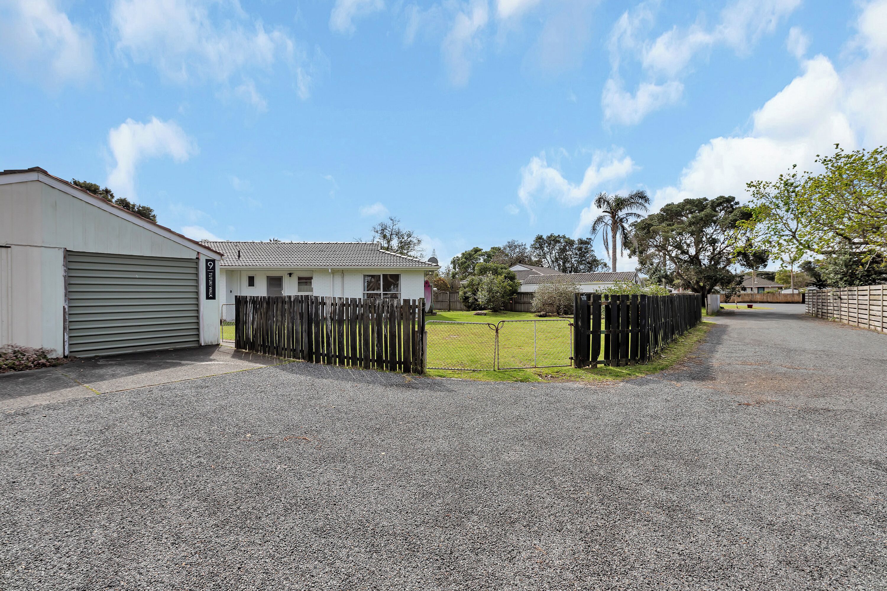 A residential property with a garage, a fenced yard, and a gravel driveway.
