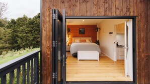 A wooden cabin with a bedroom featuring a bed, bedside table, and a bench. - Hidden Springs Retreat - Karangahake Mountain View (Waihi)