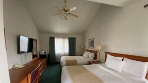 Una camera d'albergo con due letti, una scrivania con telefono, televisore e ventilatore a soffitto.