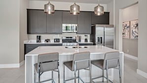 Une cuisine moderne dotée d’un grand îlot central, d’appareils électroménagers en acier inoxydable et de luminaires suspendus.
