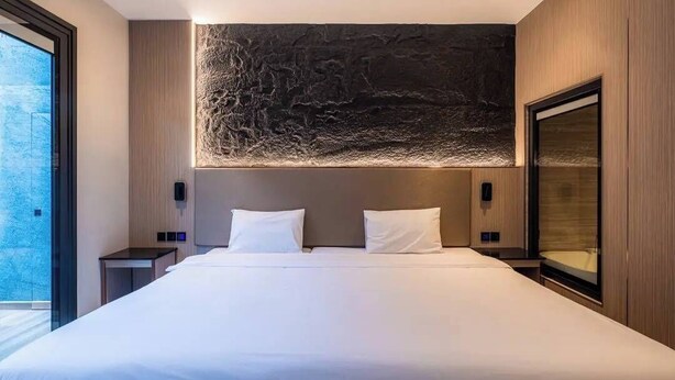 A modern hotel room with a large bed, a stone accent wall, and a large window. - Tonnam Pool Villa (Pattaya)