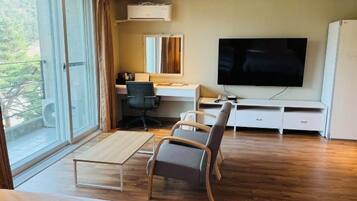 A hotel room with a large window, a desk, a chair, a television, and a wardrobe.
