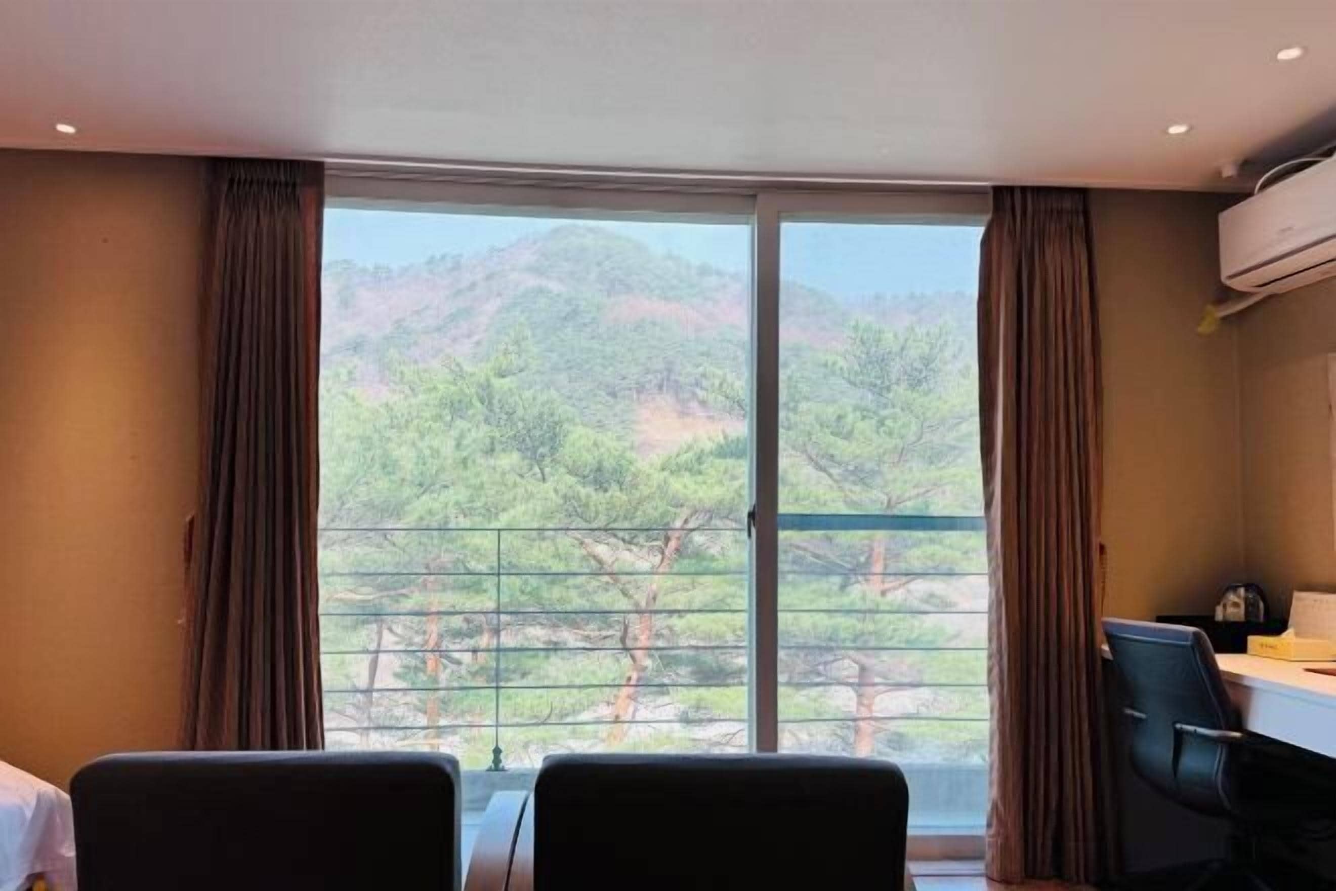 A room with a large window, two chairs, a desk, and an air conditioning unit.