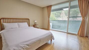 A bedroom with a bed, a nightstand, and a large window with curtains.